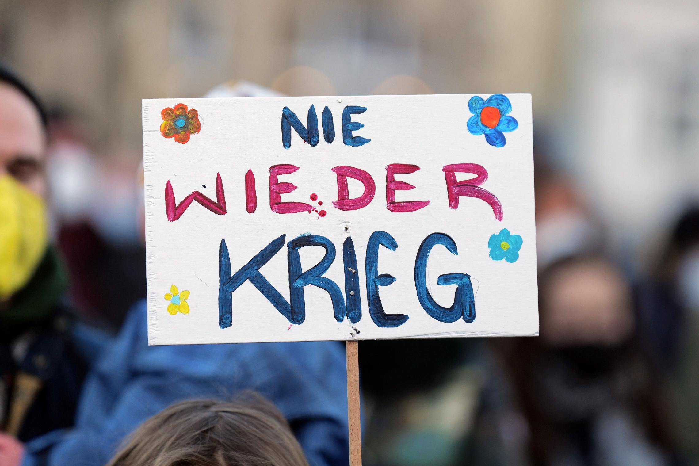 Demonstrationsschild mit der Aufschrift „Nie wieder Krieg“, umgeben von Blumenzeichnungen